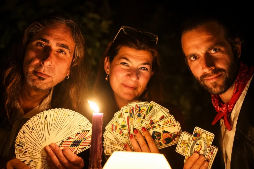 Tres tarotistas mostrando cartas de tarot iluminados por una vela en un ambiente escénico y misterioso
