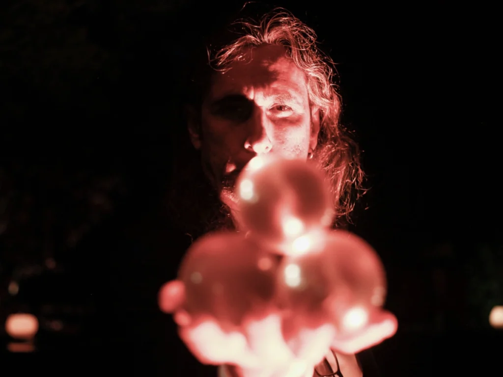 Oliverio iluminado en rojo tras varias bolas de cristal durante una experiencia de tarot